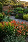 WOLLERTON OLD HALL  SHROPSHIRE. A PLACE TO SIT. METAL SEAT AND VIEW ACROSS LANHYDROCK GARDEN WITH CROCOSMIA CONSTANCE AND ERYSIMUM APRICOT DELIGHT IN FOREGROUND.