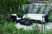 DESIGN: CHARLOTTE ROWE  LONDON.SMALL SECLUDED COUNTRY GARDEN IN JUNE WITH SOFA  TRELLIS  DIGITALIS PURPUREA ALBA  (WHITE FOXGLOVES) AND OTHER PERENNIALS WITH GLASS LANTERNS
