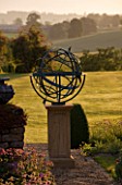 DAVID HARBER SUNDIALS: BRONZE ARMILLARY SPHERE SUNDIAL IN EVENING LIGHT WITH VIEW OF LAWN AND COUNTRYSIDE BEYOND AT PETTIFERS  OXFORDSHIRE