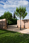 LA NORIA  FRANCE. GARDEN DESIGNED BY ARNAUD MAURIERES AND ERIC OSSART - PINE TREES AND CONCRETE WALLS BESIDE THE GARDEN ENTRANCE