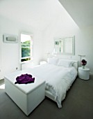 TANIA LAURIE  LONDON. WHITE BEDROOM WITH BED  BLANKET BOX AND BEDSIDE TABLE WITH VASE OF SCENTED STOCK