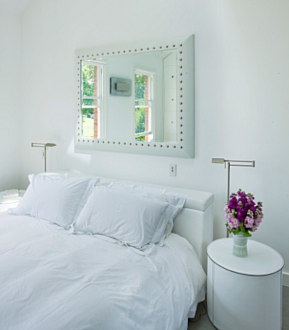 TANIA_LAURIE__LONDON_WHITE_BEDROOM_WITH_MIRROR_ABOVE_BED_AND_BEDSIDE_TABLE_WITH_VASE_OF_SCENTED_STOC