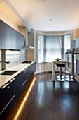 TANIA LAURIE  LONDON. CONTEMPORARY KITCHEN WITH LIGHTING  BLACK UNITS  WOODEN FLOOR AND BREAKFAST BAR