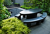 TANIA LAURIE  LONDON. SMALL CONTEMPORARY GARDEN BY CHARLOTTE ROWE WITH BLACK MARBLE OVAL TABLE AND BENCHES WITH HAKONECHLOA MACRA ALBOAUREA  HYDRANGEA AND POLISHED GREY PEBBLES