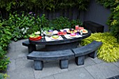 TANIA LAURIE  LONDON. LUNCH WAITING TO BE SERVED ON BLACK MARBLE TABLE AND BENCHES IN CONTEMPORARY GARDEN DESIGNED BY CHARLOTTE ROWE