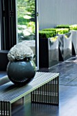 TANIA LAURIE  LONDON. CONTEMPORARY VASE AND LOW LEVEL METAL TABLE IN LIVING AREA LEADING OUT TO PATIO AREA WITH THREE BLACK METAL SQUARE CONTAINERS PLANTED WITH BOX