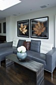 TANIA LAURIE  LONDON. CONTEMPORARY LIVING AREA WITH GREY LEATHER SOFA  METAL COFFEE TABLE WITH MODERN VASE AND LEAF PRINTS ON WALL