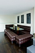 TANIA LAURIE  LONDON. INTERIOR OF DINING AREA WITH BROWN LEATHER SOFA AND STOOLS / BENCHES
