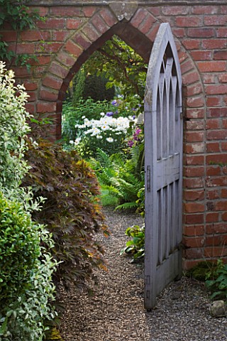 WOLLERTON_OLD_HALL__SHROPSHIREVIEW_THROUGH_BEAUTIFUL_WOODEN_GOTHIC_STYLE_GATE_WITH_PITTOSPORUM_TENUI