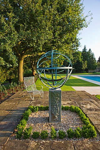 DAVID_HARBER_SUNDIALS_ARMILLARY_SPHERE_SUNDIAL_ON_STONE_PATIO_WITH_CHAIR_AND_SWIMMING_POOL_TO_THE_RI