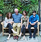 CHRIS DYSON AND FAMILY SIT ON A SEAT IN FRONT OF THE GREEN LIVING WALL