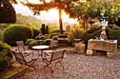 PROVENCE  FRANCE: GARDEN OF NICOLE DE VESIAN  LA LOUVE: GRAVEL TERRACE BESIDE THE HOUSE AT DAWN WITH METAL TABLE AND CHAIRS  CLIPPED TOPIARY SHAPES AND AN OLD WELL