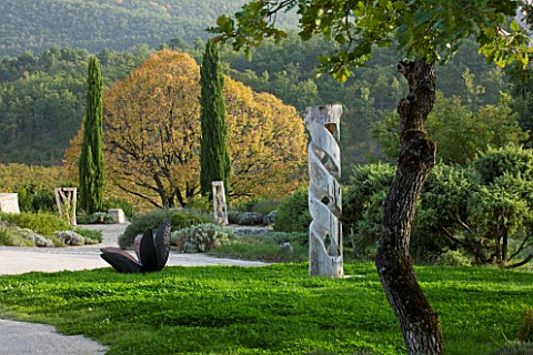 PROVENCE__FRANCE_DOMAINE_DE_LA_VERRIERE_WOODEN_SCULPTURES_BY_MARC_NUCERA_WITH_LINDEN_TREE_BEHIND