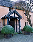 WOLLERTON OLD HALL  SHROPSHIRE: WINTER GARDEN IN FROST -  CLIPPED BOX BALLS IN HALF BARREL CONTAINERS BY THE FRONT DOOR OF THE HOUSE