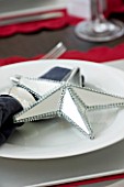 CHRISTMAS TABLE SETTING - NAPKIN AND SILVER MIRRORED STAR DECORATION ON A WHITE PLATE. SARAH EASTEL LOCATIONS/ DI ABLEWHITE