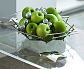 CHRISTMAS - SILVER MATAL DISH WITH GREEN APPLES AND SILVER BAUBLES ON A GLASS COFFEE TABLE. SARAH EASTEL LOCATIONS/ DI ABLEWHITE