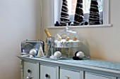 CLARE MATTHEWS CHRISTMAS HOUSE INTERIOR: DRESSER WITH SILVER RADIO  CHAMPAGNE BOTTLE  CHRISTMAS CAKE  SILVER BAUBLES WITH RIBONS