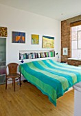 ROSE GRAY AND SCULPTOR DAVID MACILWAINE: DAVIDS ART STUDIO WITH CANVASES ON WALL BESIDE BED WITH BLUE AND GREEN BEDSPREAD