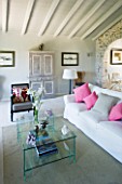 DESIGNER: CLAIRE SKINNER  ROU ESTATE  CORFU: HOUSE 11 (LAVENDULA) INTERIOR - LIVING ROOM IN GREY  CREAM AND PINK. GLASS COFFEE TABLE  SOFA WITH CUSHIONS  IRIS IN VASE