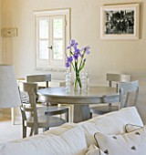 DESIGNER: CLAIRE SKINNER  ROU ESTATE  CORFU: HOUSE INTERIOR - LIVING ROOM IN GREY AND CREAM. PURPLE IRISES IN VASES  CREAM SOFA GREY WOODEN TABLE AND CHAIRS