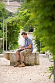 THE ROU ESTATE  CORFU: DOMINIC SKINNER SITTING ON THE WELL AT THE CENTRE OF THE VILLAGE