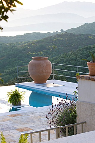 THE_KAPARELLI_ESTATE__CORFU__VIEW_OVER_SWIMMING_POOL_WITH_TERRACOTTA_URN_AND_ALBANIAN_MOUNTAINS_IN_T