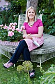 PAULA PRYKES HOUSE  SUFFOLK: PAULA RELAXES ON WHITE METAL TREE SEAT NEXT TO A TRAY OF SCENTED PELARGONIUMS