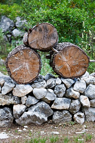 JACQUELINE_MORABITO__FRANCE__HUGE_LOGS_PILED_ON_STONE_WALL_TO_MAKE_A_SCULPTURE