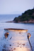CORFU  GREECE: DESIGNER: DOMINIC SKINNER - MEDITTERANEAN STYLE GARDEN  - VIEW TO WHITE TERRACOTTA CONTAINER BESIDE SWIMMING POOL WITH SEA BEYOND  LIT UP AT NIGHT  LIGHTING