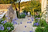 THE ROU ESTATE  CORFU  GREECE: DESIGNER: DOMINIC SKINNER - MEDITTERANEAN STYLE GARDEN - GRAVEL PATH AND AGAPANTHUS WITH THE WELL IN BACKGROUND