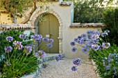THE ROU ESTATE  CORFU  GREECE: DESIGNER: DOMINIC SKINNER - MEDITTERANEAN STYLE GARDEN - GRAVEL PATH AND AGAPANTHUS WITH GREEN DOOR