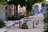 THE ROU ESTATE  CORFU  GREECE: DESIGNER: DOMINIC SKINNER - MEDITTERANEAN STYLE GARDEN - GRAVEL PATH AND AGAPANTHUS BESIDE THE WELL