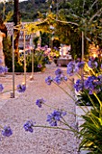 THE ROU ESTATE  CORFU  GREECE: DESIGNER: DOMINIC SKINNER - MEDITTERANEAN STYLE GARDEN - GRAVEL PATH  WELL AND AGAPANTHUS LIT UP AT NIGHT. LIGHTING