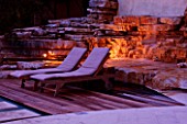 THE ROU ESTATE  CORFU  GREECE: DESIGNER: DOMINIC SKINNER - THE SWIMMING POOL AREA LIT UP AT NIGHT. THE WATERFALL AND SUN LOUNGERS. LIGHTING