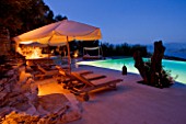 THE ROU ESTATE  CORFU  GREECE: DESIGNER: DOMINIC SKINNER - THE SWIMMING POOL AREA  LIT UP AT NIGHT WITH SUN LOUNGERS. LIGHTING