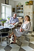 DESIGNER: ANNE FOWLER - THE KITCHEN - ALAN  AND ANNE FOWLER SITTING BESIDE THE TABLE