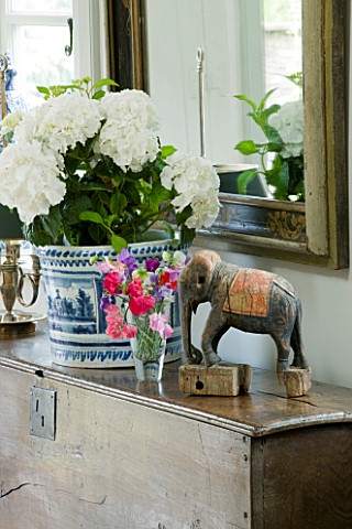 DESIGNER_ANNE_FOWLER__THE_LIVING_ROOM__DETAIL_OF_WOODEN_CABINET_WITH_ELEPHANT__SWEET_PEAS_AND_CONTAI