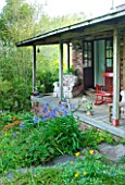 MOORS MEADOW GARDEN & NURSERY  HEREFORDSHIRE: VERANDA AND DECKING AT BACK OF HOUSE WITH CHAIR  SETTEES  AGAPANTHUS AND CROCOSMIA