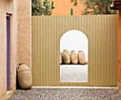 DESIGNERS ERIC OSSART AND ARNAUD MAURIERES  MOROCCO:  AL HOSSOUN - COURTYARDS WITH WOODEN FENCE AND GATEWAY/ ENTRANCEWAY FRAMING TERRACOTTA CONTAINERS