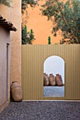 DESIGNERS ERIC OSSART AND ARNAUD MAURIERES  MOROCCO:  AL HOSSOUN - COURTYARDS WITH WOODEN FENCE AND GATEWAY/ ENTRANCEWAY FRAMING TERRACOTTA CONTAINERS
