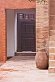 DESIGNERS ERIC OSSART AND ARNAUD MAURIERES  MOROCCO: AL HOSSOUN - COURTYARD WITH STAIRCASE  TERRACOTTA CONTAINER AND ARCH TO WOODEN DOORWAY