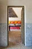 DESIGNERS ERIC OSSART AND ARNAUD MAURIERES  MOROCCO: AL HOSSOUN - VIEW INTO LIVING ROOM WITH ORANGE AND YELLOW CUSHIONS ON SETTEE