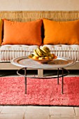 DESIGNDESIGNERS ERIC OSSART AND ARNAUD MAURIERES  MOROCCO: AL HOSSOUN - LIVING ROOM WITH ORANGE CUSHIONS ON SETTEE - ROUND TABLE WITH FRUIT BOWL