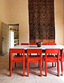 DESIGNERS ERIC OSSART AND ARNAUD MAURIERES  MOROCCO: AL HOSSOUN - DINING TABLE WITH RED CHAIRS AND CARPET ON WALL
