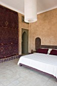 DESIGNERS ERIC OSSART AND ARNAUD MAURIERES  MOROCCO: AL HOSSOUN - BEDROOM WITH WOODN BED  MAGENTA CUSHIONS AND CARPET ON WALL