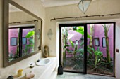 DESIGNERS ERIC OSSART AND ARNAUD MAURIERES  MOROCCO: AL HOSSOUN - BATHROOM WITH VIEW OUT TO GARDEN WITH PURPLE WALL