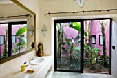 DESIGNERS ERIC OSSART AND ARNAUD MAURIERES  MOROCCO: AL HOSSOUN - BATHROOM WITH VIEW OUT TO GARDEN WITH PURPLE WALL