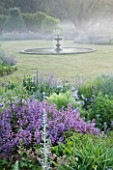 NARBOROUGH HALL GARDENS  NORFOLK: DAWN LIGHT ON THE FOUNTAIN IN THE LAWN WITH BLUE BORDERS AROUND