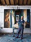 THE HOUSE OF JOHN AND SUE MONKS  LONDON: JOHN IN HIS STUDIO BESIDE AN OIL PAINTING