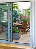 LONDON ROOFTOP GARDEN: SHUTTERED SLIDING DOORS LEADING TO GARDEN ROOM. LIMESTONE FLOOR  WOODEN TABLE AND CHAIRS  AGAPANTHUS UMBELLATUS OVATUS